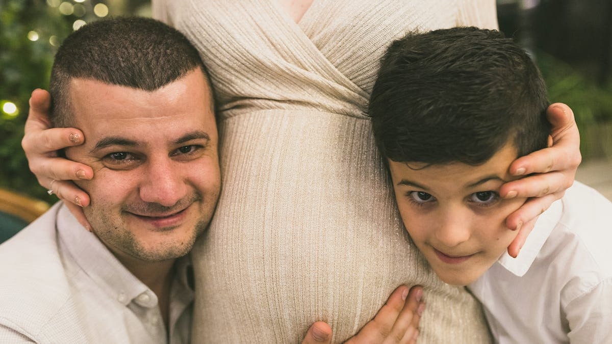 A joyful family moment with father and son embracing the pregnant mother, symbolizing love and togetherness.